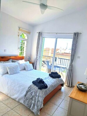 Quarto de hotel com cama, ventilador de teto, janela com cortinas e vista para o exterior.
