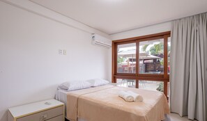 A hotel room with a bed, a nightstand, a window with curtains, and an air conditioning unit on the wall.