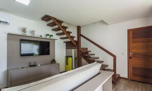 Uma sala de estar moderna com escada de madeira, televisão de tela plana, painel de entretenimento embutido e uma porta.