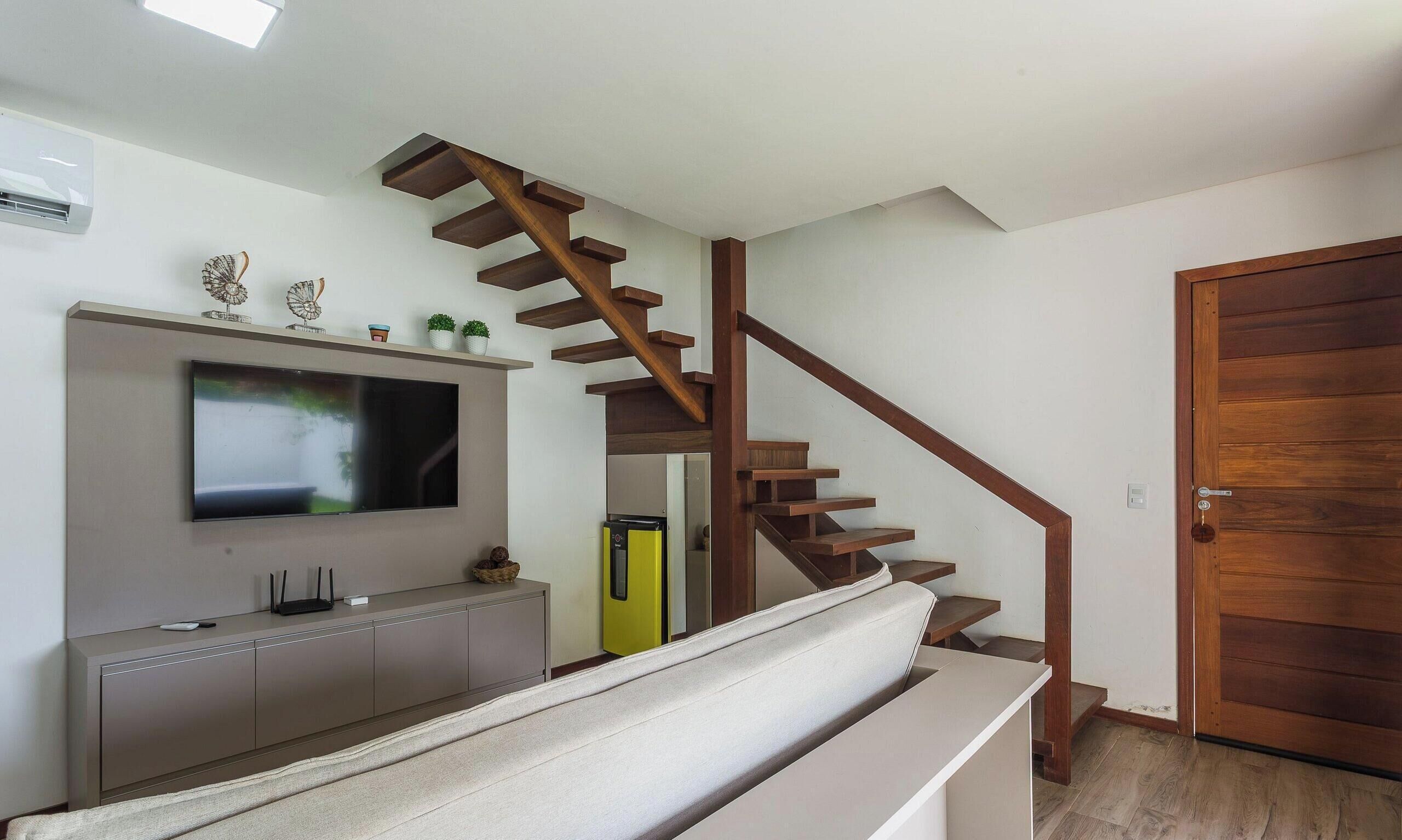 Een moderne woonkamer met een houten trap, een flatscreen televisie en een inbouwmeubel.