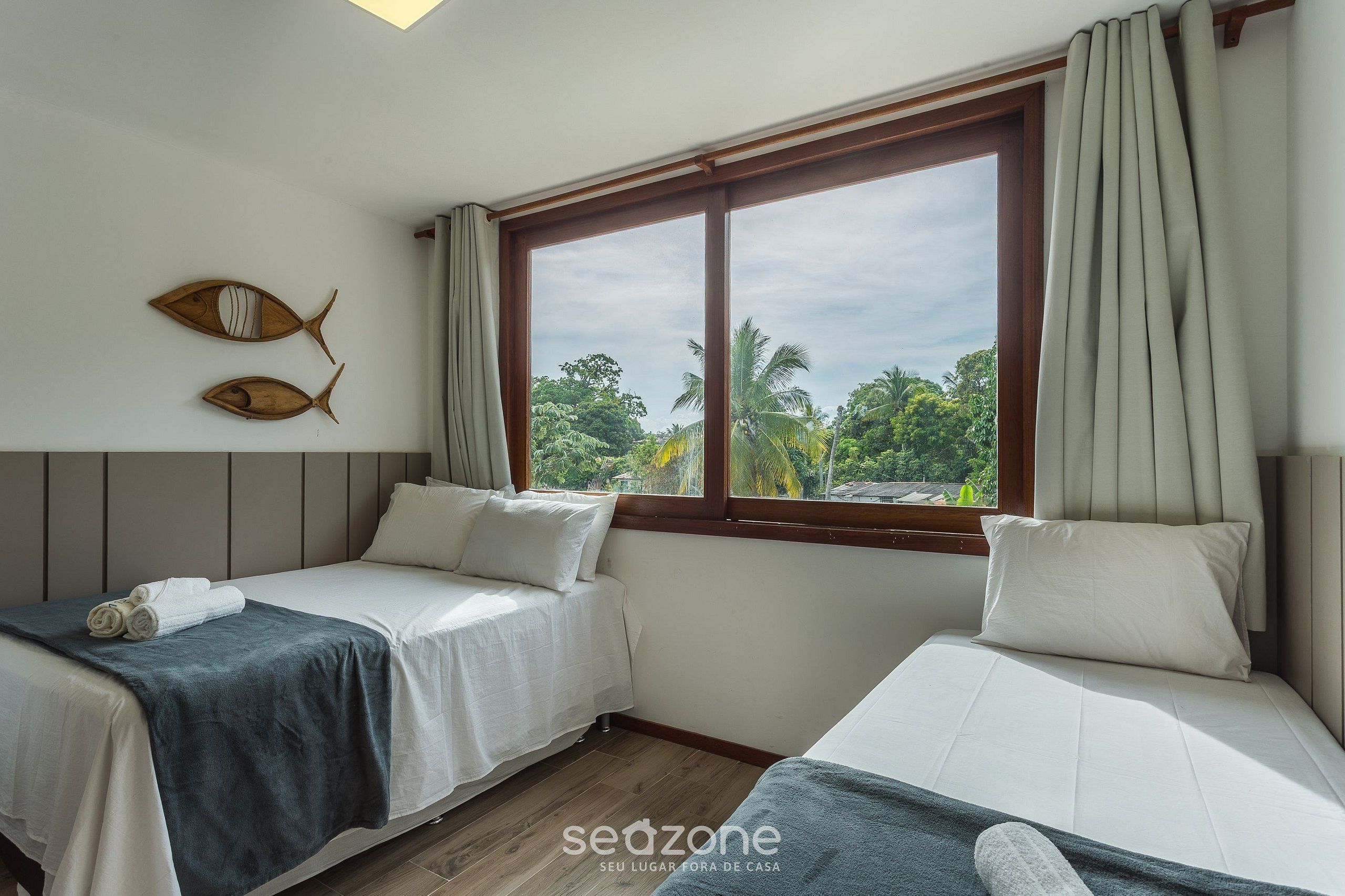Une chambre avec deux lits, une grande fenêtre avec des rideaux et une vue sur la verdure.