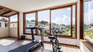 En rummelig balkon med løbebånd og motionscykel, store vinduer der giver udsigt over et boligområde.