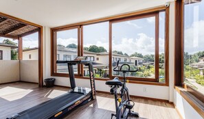 Ein geräumiger Balkon mit Laufband und stationärem Fahrrad, große Fenster mit Blick auf eine Wohngegend.