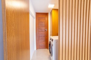 Ein schmaler Flur mit einer Holztür am Ende und einer Waschmaschine zur Rechten.