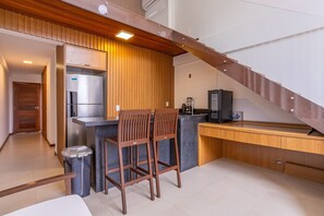 Eine moderne Küche mit Holzschränken, einem Edelstahlkühlschrank, einer Kaffeemaschine und einer Bar mit zwei Hockern.