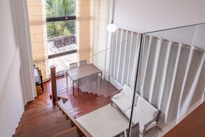 Eine Treppe führt zu einem Balkon mit einem Holztisch, Stühlen, einem weißen Sofa und einer hängenden Lampe.