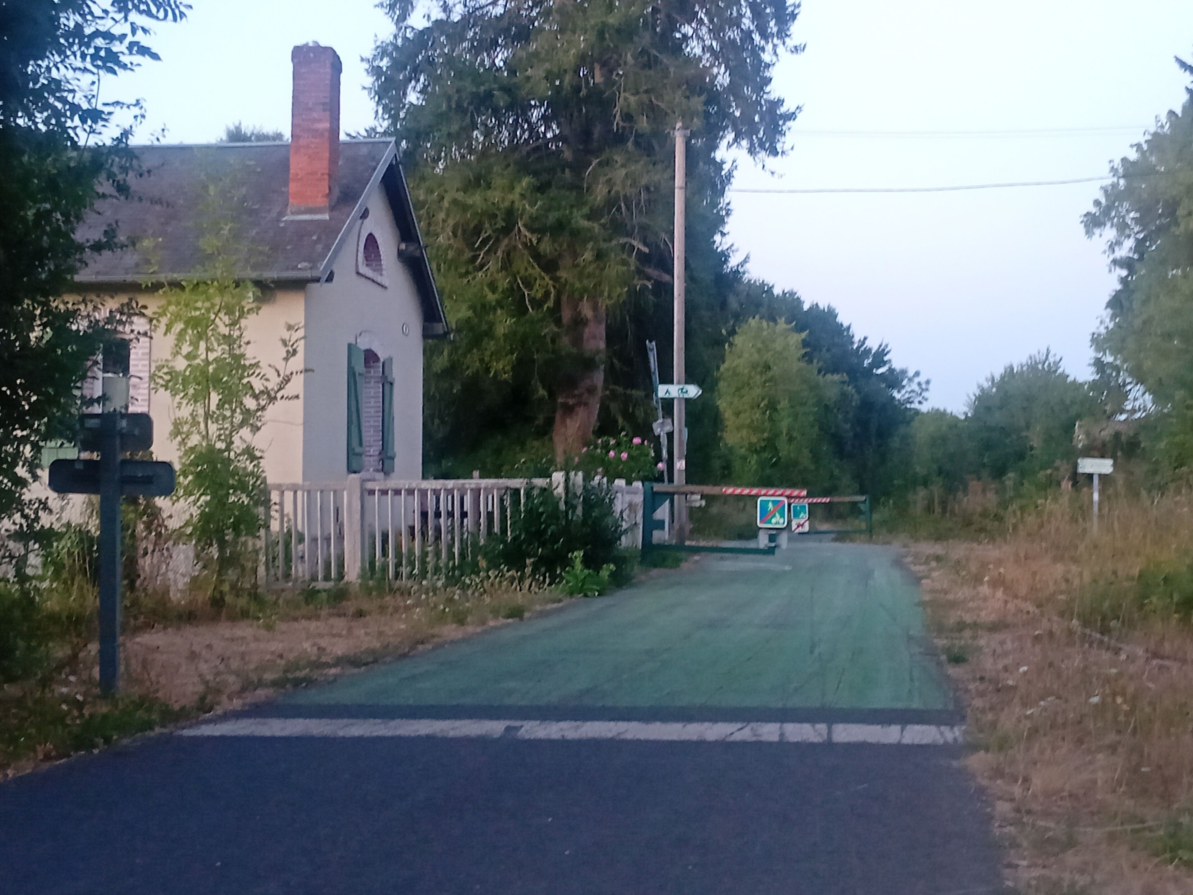 Una carretera rural con una casa blanca, un portón verde y una señalizadora.