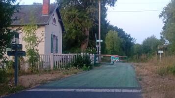 Una carretera rural con una casa blanca, un portón verde y una señalizadora.