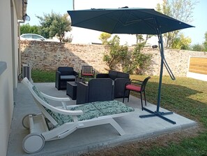 A patio with outdoor furniture, including a lounge chair and a dining set, under a large umbrella. - New home between the sea and the Swiss Normandy region (Feuguerolles-Bully)