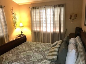 Ett hotellrum med en säng, gardiner, en lampa, en kristallkrona och en telefon som är monterad på väggen.