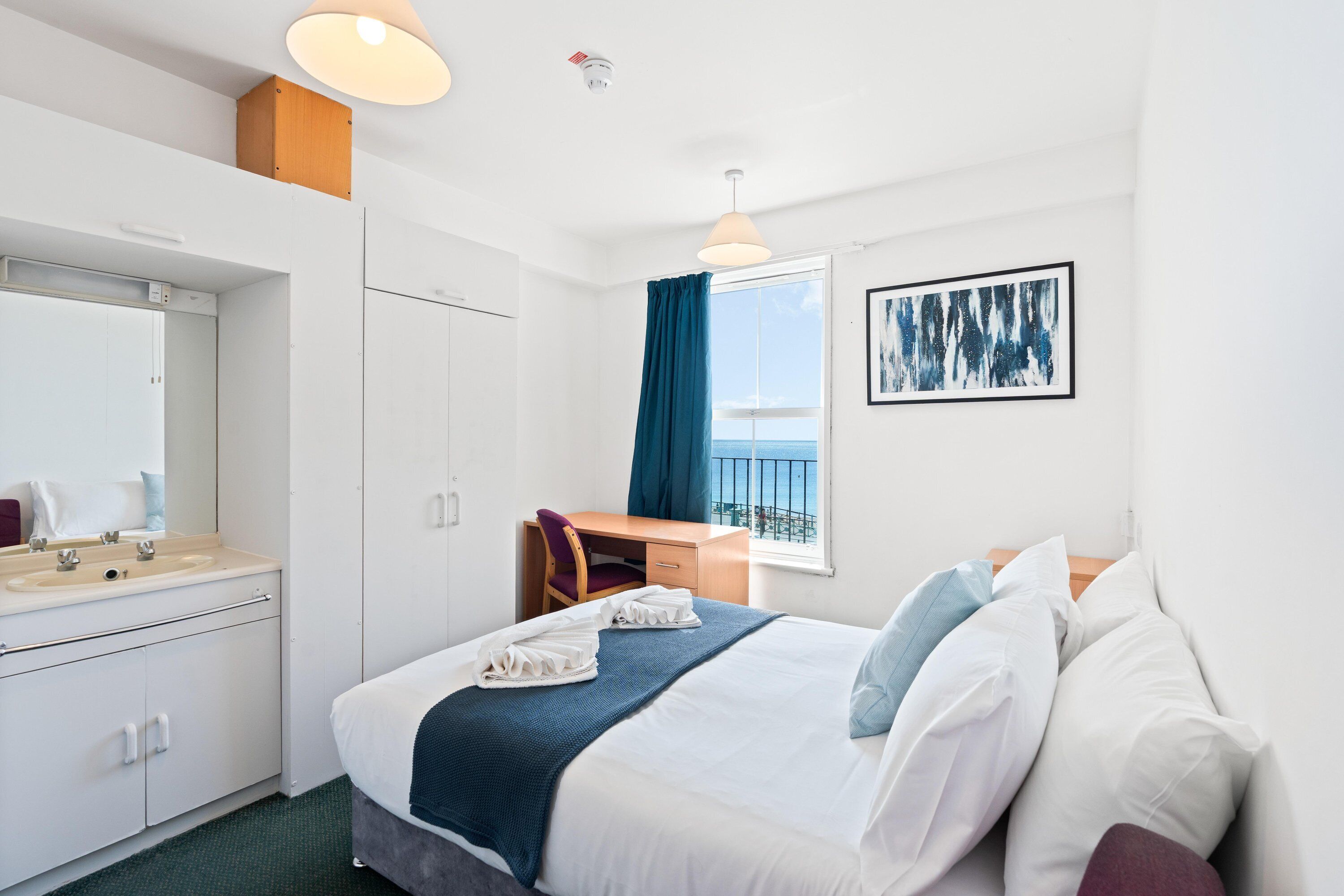 A hotel room with a bed, a desk, a chair, a window with a view, and a bathroom.