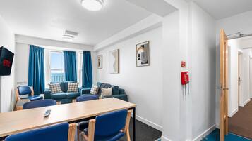 A hotel room with a sofa, chairs, a table, a TV, and a window with curtains.