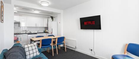 A modern living room with a sofa, a TV mounted on the wall, and a kitchen in the background.