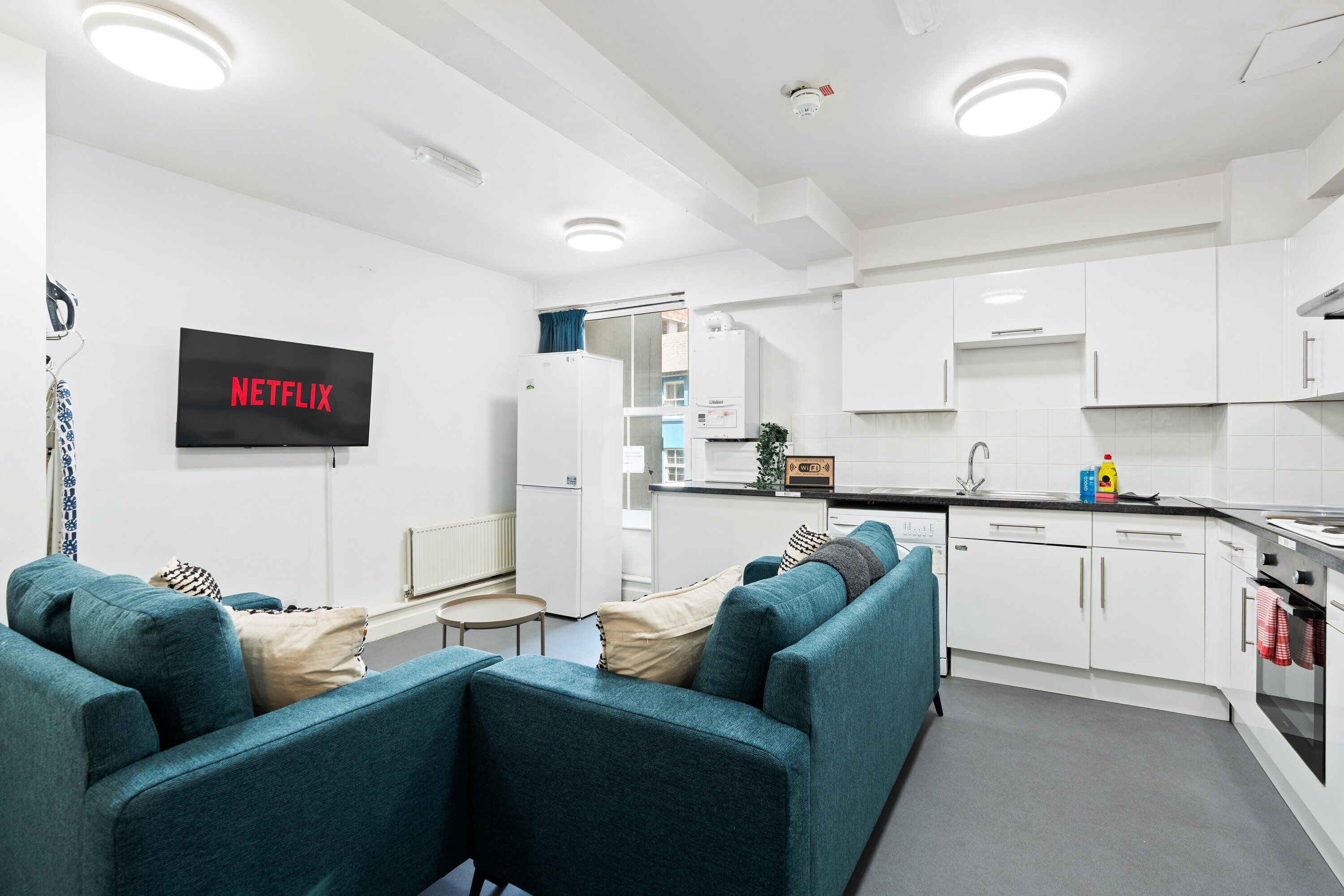 A modern kitchen with white cabinets, a built-in oven, and a sink. There is a flat-screen TV mounted on the wall with 'NETFLIX' displayed.
