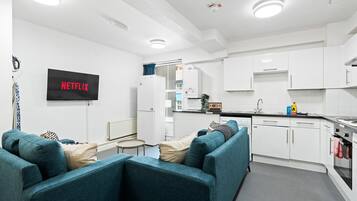A modern kitchen with white cabinets, a built-in oven, and a sink. There is a flat-screen TV mounted on the wall with 'NETFLIX' displayed.
