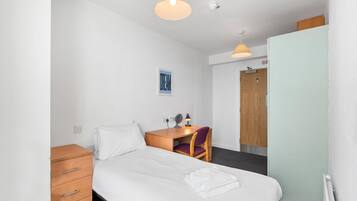 A hotel room with a bed, a desk, a chair, a wardrobe, and a ceiling-mounted fan.