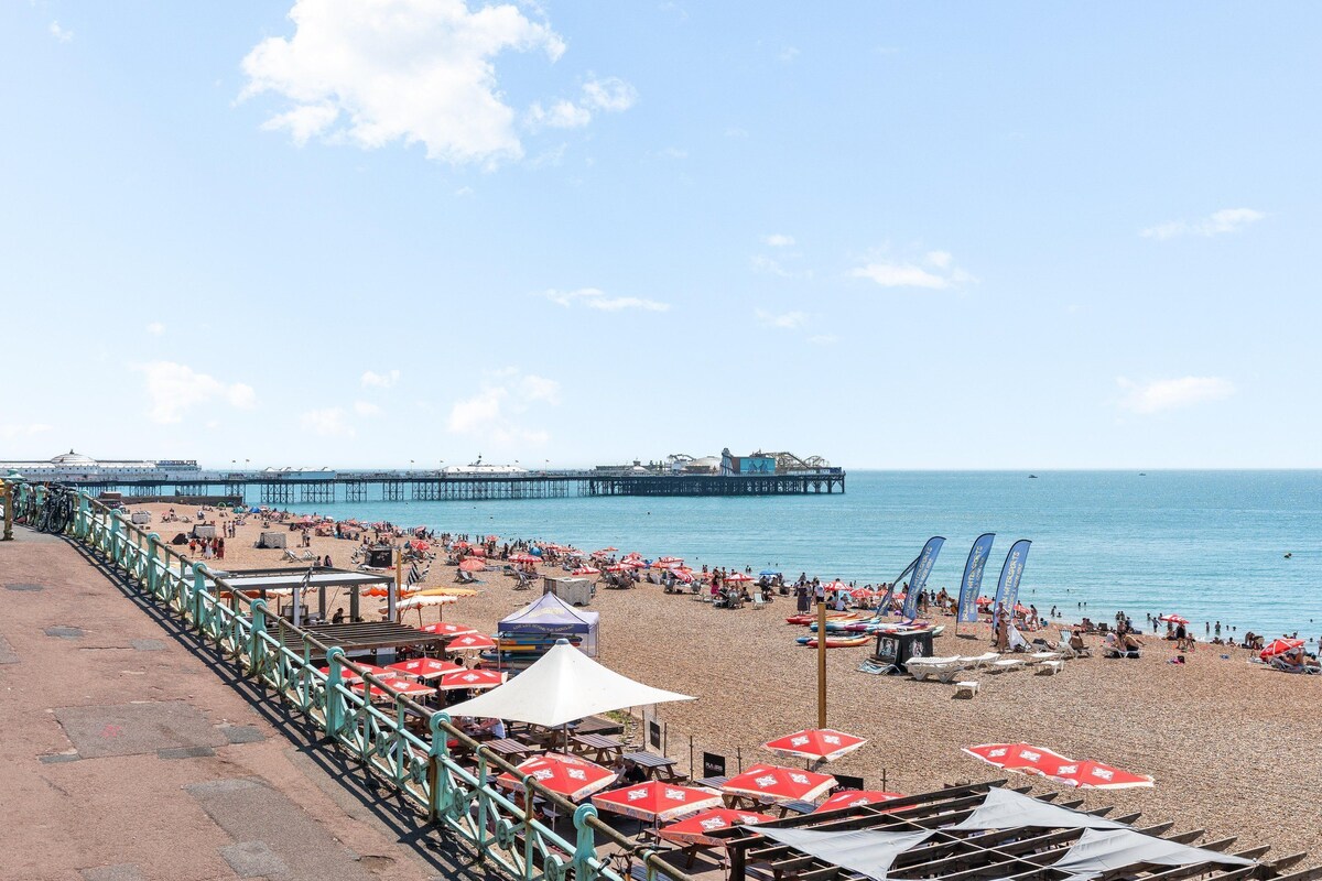 A beach with umbrellas, chairs, and a pier in the background.