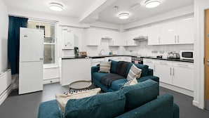 A modern kitchen with white cabinets, a dining area with a teal sofa, and a small round table.