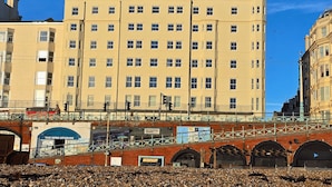 A multi-story building with a flat facade, numerous windows, and a pedestrian bridge with a metal railing.