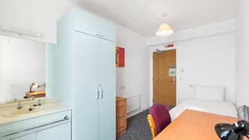 A hotel room with a bed, a desk, a chair, a wardrobe, a bathroom, and a door with a 'No Smoking' sign.