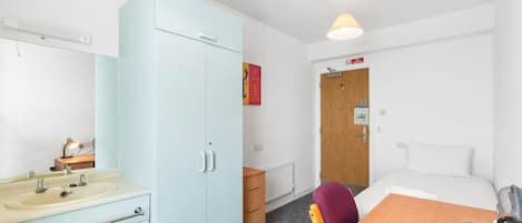 A hotel room with a bed, a desk, a chair, a wardrobe, a bathroom, and a door with a 'No Smoking' sign.