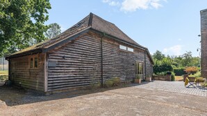 Un edificio rústico de madera con techo inclinado, camino de grava y una pequeña zona exterior con mesa y sillas.