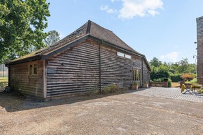 A rustic wooden building with a sloped roof, a gravel driveway, and a small outdoor seating area with a table and chairs. - Medleys Barn By My Getaways (Uckfield)