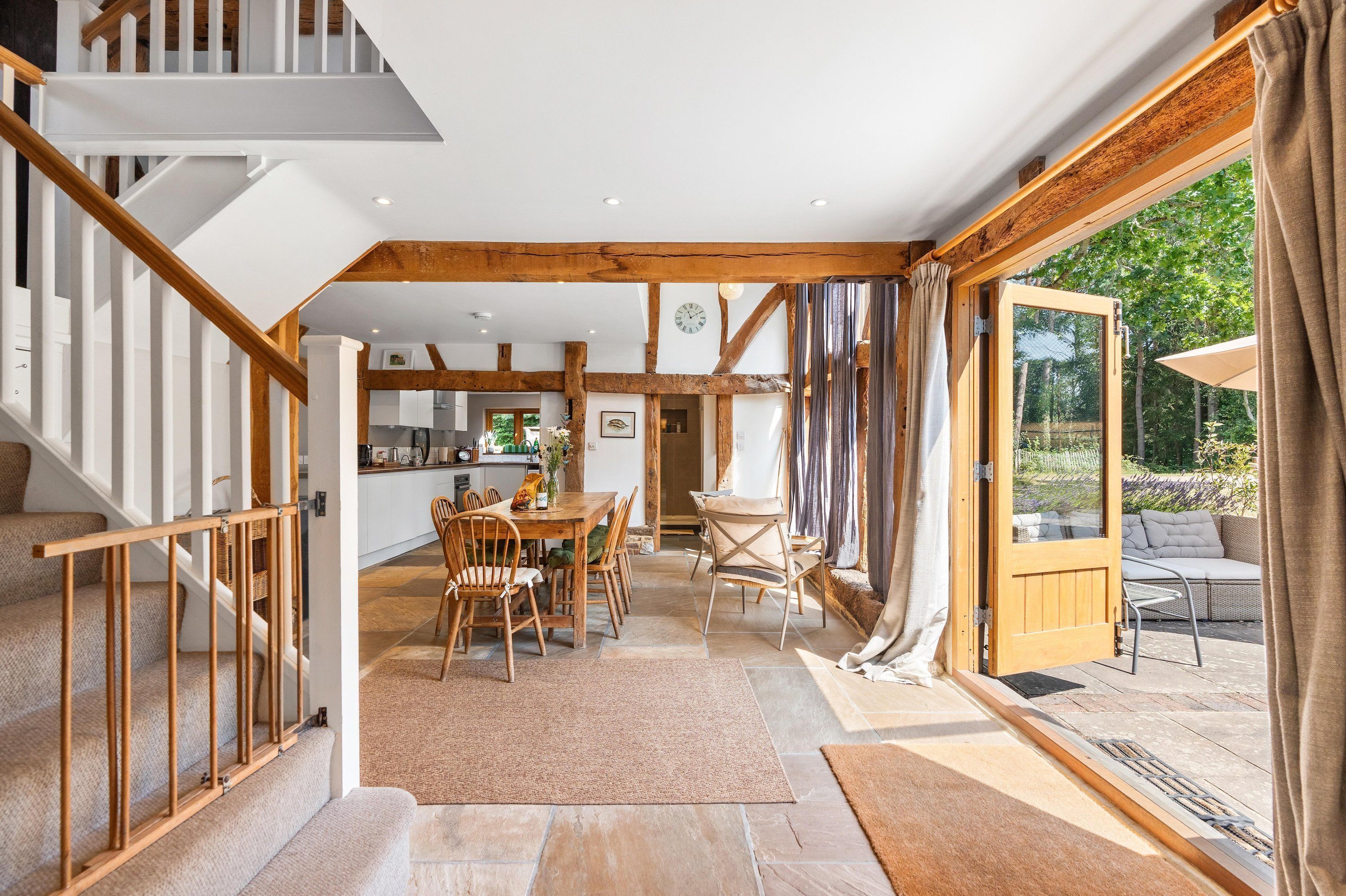 Un ambiente spazioso con una scala in legno, un'area pranzo e vista su un'area salotto esterna attraverso un'ampia porta in vetro.