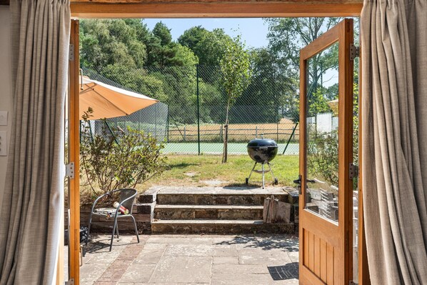 Une porte ouverte donne sur un patio équipé d’un barbecue, d’une chaise pliante et d’une table abritée.