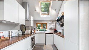 Cocina compacta con armarios blancos, encimera de madera, lavavajillas integrado y ventana que proporciona luz natural.
