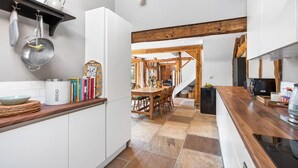 Una cocina moderna con zona de comedor de madera, estufa integrada y diversos utensilios y electrodomésticos.