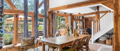 Un comedor amplio con una mesa y sillas de madera, ventanas grandes y una escalera que sube a un nivel superior.