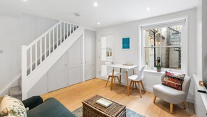 A modern interior with a staircase, white furniture, a dining area, and a window with a view of an outdoor staircase. - Bloomsbury Snug By My Getaways (Brighton)