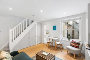 Ein modernes Interieur mit einer Treppe, weißen Möbeln, einem Essbereich und einem Fenster mit Blick auf eine Außentreppe.