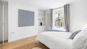 A modern bedroom with a large bed, a wall-mounted artwork, a radiator, and a window with curtains. - Bloomsbury Snug By My Getaways (Brighton)