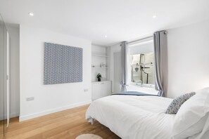 Ein modernes Schlafzimmer mit einem großen Bett, einem Wandbild, einem Heizkörper und einem Fenster mit Vorhängen.