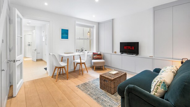 A modern living room with a flat-screen TV, a sofa, and a dining area with chairs. - Bloomsbury Snug By My Getaways (Brighton)