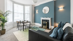 A living room with a fireplace, a dining area with a table and chairs, and a large window. - Seaside Haven in Brighton (Brighton)