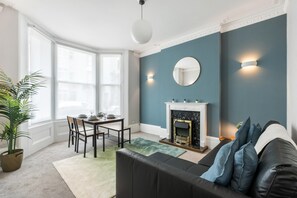A living room with a fireplace, a dining area with a table and chairs, and a large window. - Seaside Haven in Brighton (Brighton)