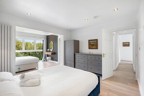 Ein Schlafzimmer mit einem großen Bett, einem Schminktisch, einem Spiegel und Blick auf Grünflächen außerhalb.