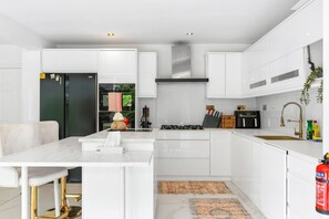A modern kitchen with white cabinetry, a central island, a gas stove, and a stainless steel sink. - Downs Heights By My Getaways (Brighton)
