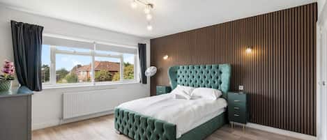 Un dormitorio con una cama grande, una ventana, un radiador y un panel de pared de madera.
