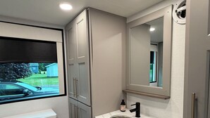 A modern bathroom with a large window, a sink, and cabinets. - The Coastal Caravan (Alberton)
