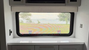 A compact RV interior with a flat-screen TV mounted above a window, a fireplace below, and a small storage area with drawers. - The Coastal Caravan (Alberton)