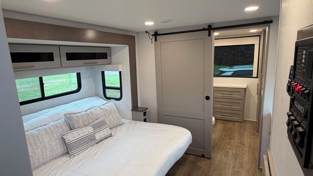 A bedroom with a bed, a TV, and a door leading to a bathroom. - The Coastal Caravan (Alberton)