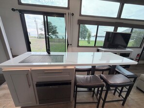 A kitchen with a large island, a built-in oven, and a view of the outdoors through large windows.
