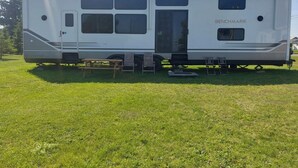 A white RV with the brand 'BENCHMARK' visible on the side, equipped with a sliding door and multiple windows. - The Coastal Caravan (Alberton)