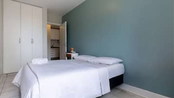 Un dormitorio con cama, ropa de cama blanca, un armario y una pared verde azulado.