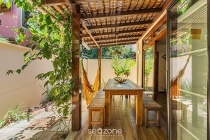 Una veranda riparata con tavolo e panche in legno, circondata da piante e una porta vetrata.