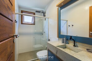 Un bagno con box doccia in vetro, un water bianco e un piano in granito con rubinetto nero.